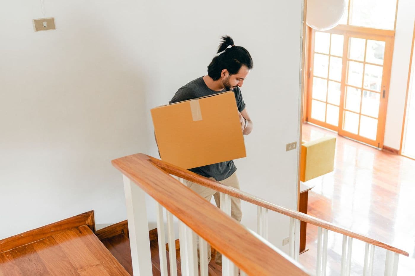 A man carrying a cardboard box up the stairs of a home